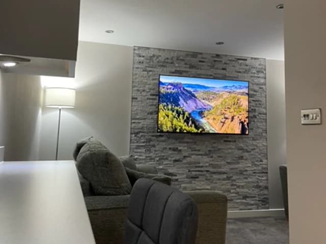 Garden room interior with a grey sofa, television and textured feature wall